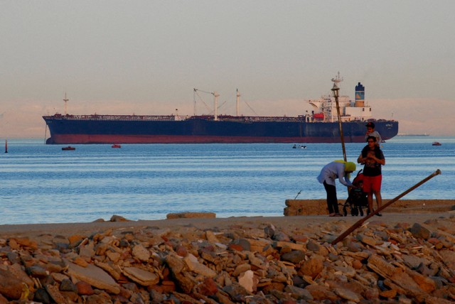 Orang-orang berjalan di pantai saat kapal kontainer melintasi Teluk Suez menuju Laut Merah sebelum memasuki Terusan Suez, di El Ain El Sokhna di Suez, timur Kairo, Mesir 24 April 2017. Foto: Amr Abdallah Dalsh/REUTERS