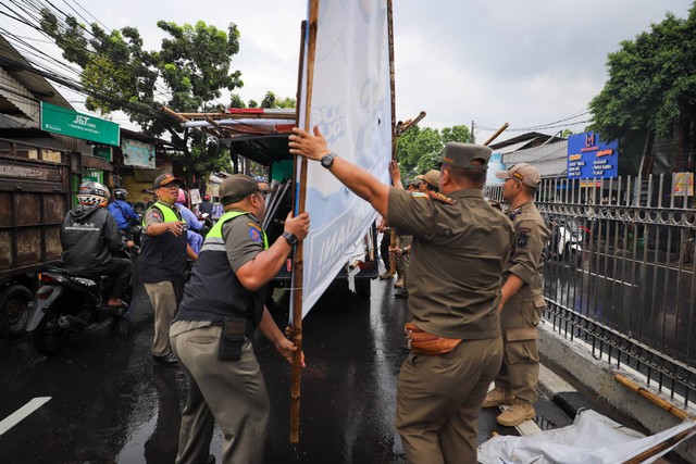 Sejumlah personel Satpol PP menertibkan alat peraga kampanye (APK) di kawasan Jalan Raya Bogor, Kramat Jati, Jakarta, Senin (29/1/2024). Foto: Iqbal Firdaus/kumparan