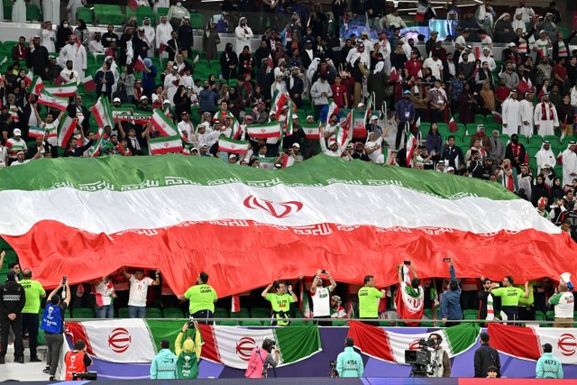 Suporter Iran memegang bendera nasional raksasa negara mereka selama pertandingan semi final Piala Asia 2023 antara Iran dan Qatar di Stadion Al Thumama, Doha, Qatar, pada 7 Februari 2024. Foto: Hector RETAMAL / AFP