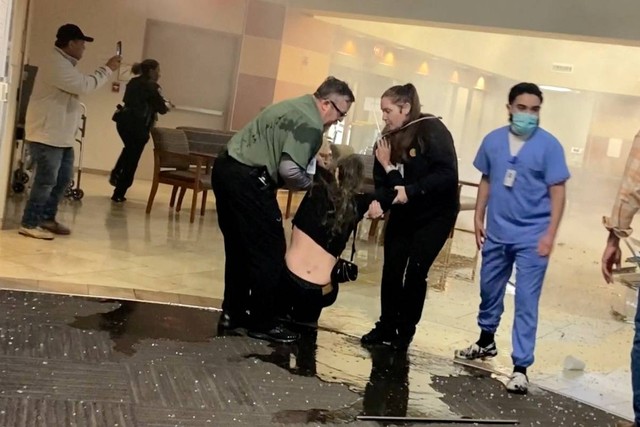 Seorang wanita menggendong seorang anak berdiri di dekat asap yang mengepul dari lokasi di mana sebuah kendaraan melaju ke ruang gawat darurat di St. David's North Austin Medical Center di Austin, Texas, AS, Selasa (13/2/2024). Foto: Stephen Hughes/via REUTERS