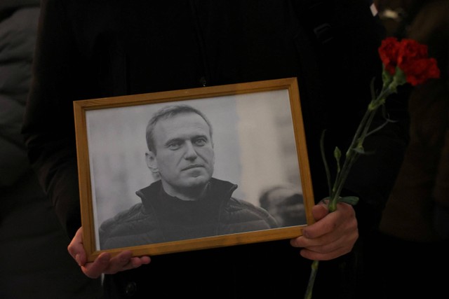 Seseorang memegang bunga dan potret pemimpin oposisi Rusia Alexei Navalny di monumen korban penindasan politik setelah kematian Navalny, di Saint Petersburg, Rusia, Jumat (16/2/2024). Foto: STR/REUTERS