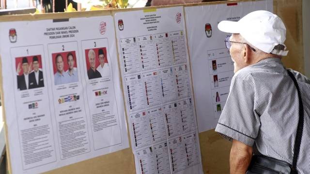 Seorang warga lansia melihat papan pengumuman di salah satu TPS pada Pemilu 2024. (foto: febry kodongan)