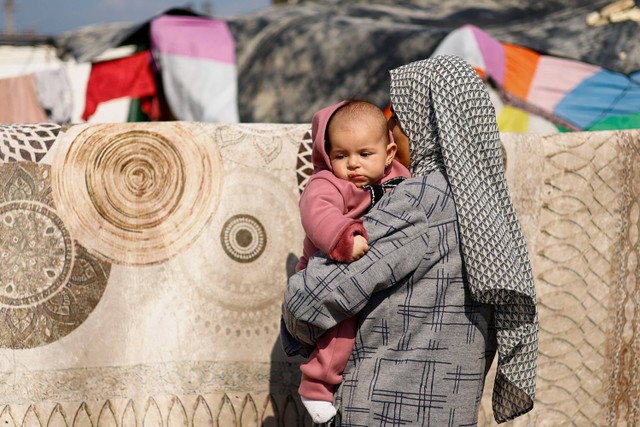 Seorang wanita menggendong bayi, saat warga Palestina yang mengungsi, yang meninggalkan rumah mereka akibat serangan Israel, berlindung di tenda kamp di tengah konflik yang sedang berlangsung antara Israel dan Hamas, di Rafah di Jalur Gaza selatan. Foto: Mohammed Salem/Reuters