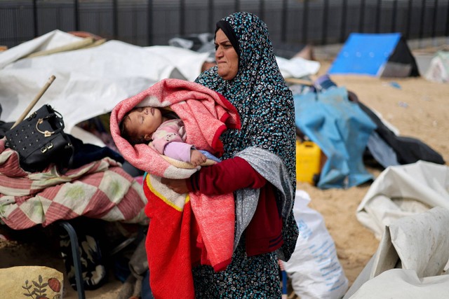 Seorang wanita menggendong bayi ketika warga Palestina yang melarikan diri dari Khan Younis akibat operasi darat Israel tiba di Rafah, di tengah konflik yang sedang berlangsung antara Israel dan kelompok Islam Palestina Hamas, di Jalur Gaza selatan. Foto: Mohammed Salem/Reuters