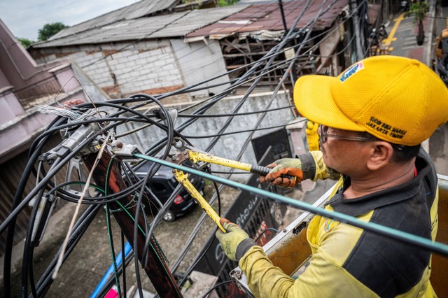 Seorang petugas Suku Dinas Bina Marga DKI Jakarta memotong kabel utilitas di Jalan Raya Bekasi, Jakarta, Senin (26/2/2024). Foto: Bayu Pratama S/Antara Foto