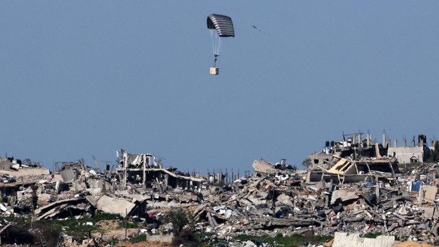 Gambar yang diambil dari posisi di Israel selatan pada tanggal 29 Februari 2024, menunjukkan parasut milik Tentara Israel menjatuhkan sebuah kotak di atas bangunan yang hancur di Jalur Gaza, di tengah pertempuran yang sedang berlangsung. Foto: Jack Guez / AFP