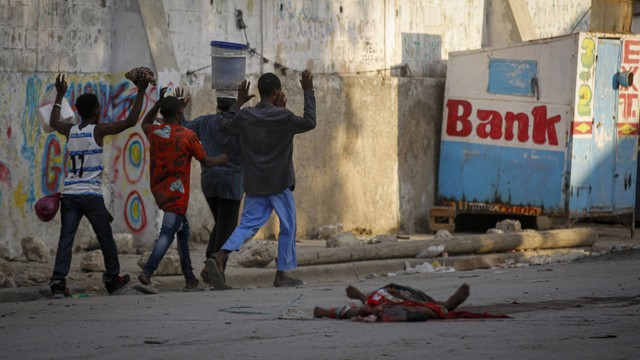 Warga berjalan melewati jenazah pria saat bentrokan antara polisi dan anggota geng di lingkungan Portail di Port-au-Prince di Port-au-Prince, Haiti, Kamis, 29 Februari 2024. Foto: AP/Odelyn Joseph