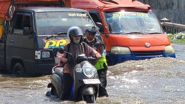 Anggota Satlantas Polrestabes Semarang membantu seorang pengendara sepeda motor yang terjebak banjir di sekitar Jalan Kaligawe Semarang, Jawa Tengah, Sabtu (6/4/2024). Foto: I.C. Senjaya/ANTARA