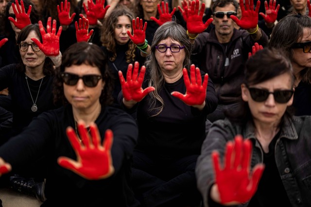 Keluarga bersama para pendukung aksi membentuk jam pasir dan mengecat tangan mereka berwarna merah di Tel Aviv, Israel, Minggu (7/4/2024) Foto: Ariel Schalit/AP Photo