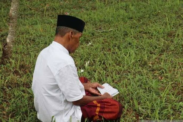 Salah satu warga membaca Al quran di kawasan kuburan massal tsunami Aceh. Rabu (10/4/2024) Foto: Rahmat Fajri/Antara