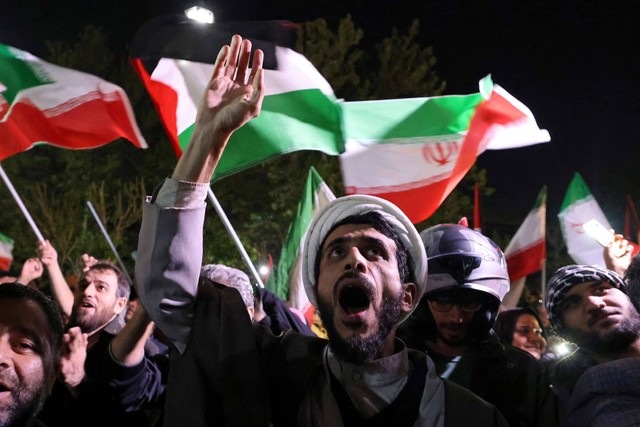 Demonstran mengibarkan bendera Iran saat mereka berkumpul di depan Kedutaan Besar Inggris di Teheran, Minggu (14/4/2024). Foto: ATTA KENARE / AFP