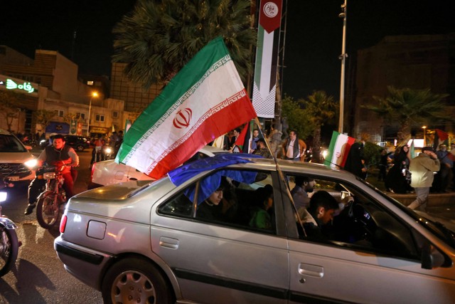 Demonstran mengibarkan bendera Iran menggunakan mobil saat mereka berada di kawasan Kedutaan Besar Inggris di Teheran, Minggu (14/4/2024). Foto: ATTA KENARE / AFP