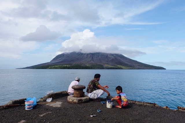 Orang-orang memancing di pelabuhan di Pulau Tagulandang di Sitaro, Sulawesi Utara, Jumat (19/4/2024). Tampak di depannya Gunung Ruang. Foto: Ronny Adolof BUOL / AFP