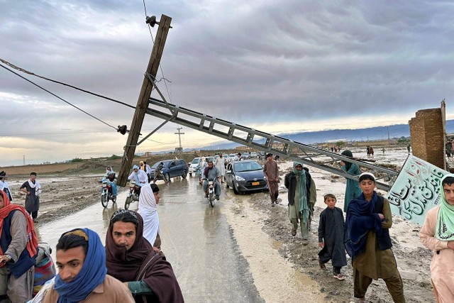 Orang-orang melewati tiang listrik yang rusak akibat banjir akibat hujan lebat di dekat daerah Chaman, Pakistan, Kamis, (18/4/2024). Foto: Habib Ulla/AP PHOTO