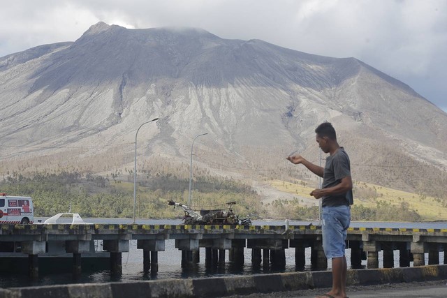 Seorang warga tampak memancing di area Pelabuhan Tagulandang dengan latar belakang Gunung Ruang di seberang pulau. (foto: febry kodongan/manadobacirita)
