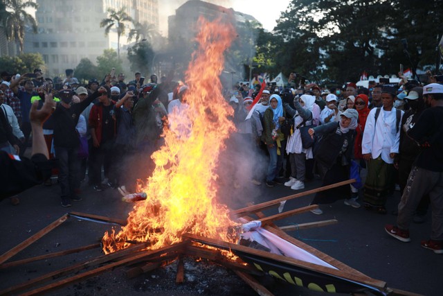 Massa pendukung paslon 01 dan 03 membakar spanduk bergambar Jokowi saat menggelar aksi unjuk rasa di sekitar Patung Kuda di sela mengawal keputusan Mahkamah Konstitusi pada Senin (22/4/2024) Foto: Aditia Noviansyah/kumparan