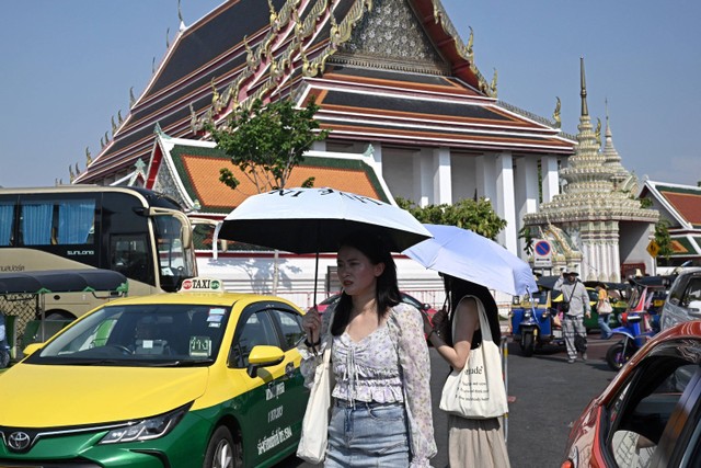 Wisatawan melindungi diri dari sinar matahari dengan payung di luar kuil Buddha Wat Pho di Bangkok, Thailand, pada 1 April 2024. Foto: LILLIAN SUWANRUMPHA / AFP