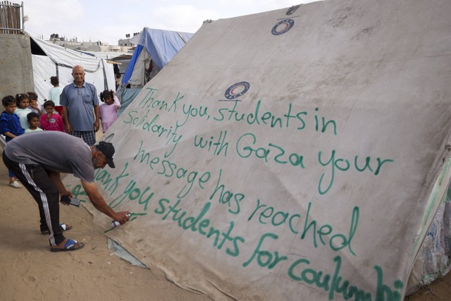 Seorang pria menulis pesan terima kasih kepada mahasiswa di AS yang melakukan protes solidaritas terhadap rakyat Gaza, di tenda di kamp pengungsi Palestina di Rafah, di Jalur Gaza selatan pada 27 April 2024, di tengah konflik yang sedang berlangsung. Foto: Dimitar DILKOFF / AFP
