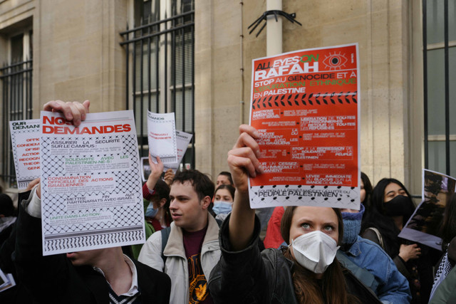 Para pengunjuk rasa mengangkat poster bertuliskan "Tuntutan kami" (kiri) dan "Semua mata tertuju pada Rafah" ketika mahasiswa menduduki gedung Institut Studi Politik (alias Sciences Po) untuk mendukung Palestina, di Paris pada 26 April 2024. Foto: Dimitar DILKOFF / AFP