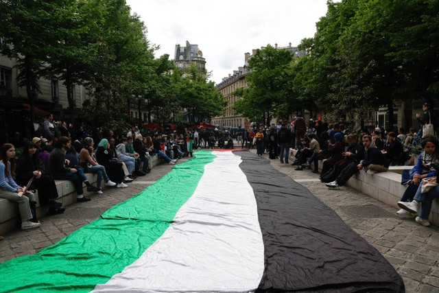 Mahasiswa duduk di samping bendera raksasa Palestina yang dikibarkan di depan Universitas Sorbonne selama unjuk rasa mendukung Palestina, di Paris (29/4/2024) Foto: Geoffroy VAN DER HASSELT / AFP
