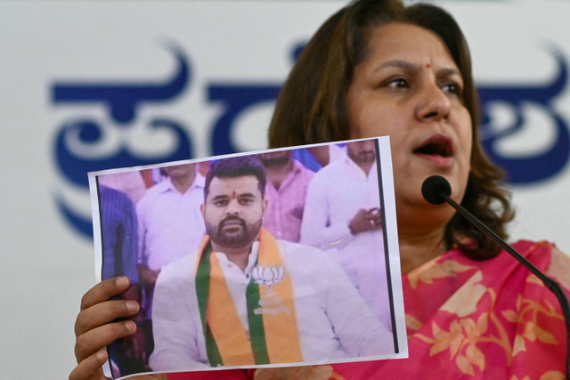 Juru bicara Kongres Supriya Shrinate menunjukkan foto yang menampilkan anggota parlemen JD(S) Prajwal Revanna (kiri) yang dipanggil karena dugaan kasus pelecehan seksual, pada konferensi pers di Bengaluru pada 1 Mei 2024. Foto: Idrees Mohammed / AFP