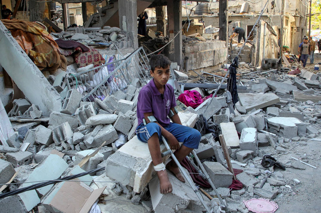 Seorang anak Palestina yang terluka duduk di atas puing-puing di lokasi serangan Israel terhadap sebuah rumah, di tengah konflik antara Israel dan Hamas, di Rafah, di selatan Jalur Gaza, Kamis (9/5/2024). Foto: Hatem Khaled/REUTERS