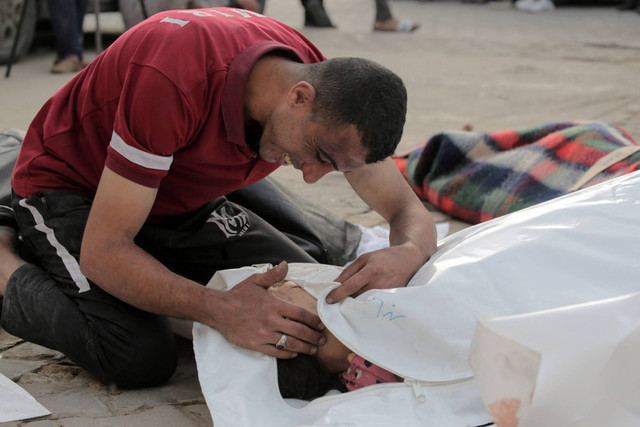 Seorang pria Palestina bereaksi terhadap jenazah seorang anak yang tewas dalam pemboman Israel, di halaman Rumah Sakit Martir Al-Aqsa di Deir al-Balah di Jalur Gaza tengah pada Sabtu (11/5/2024). Foto: AFP