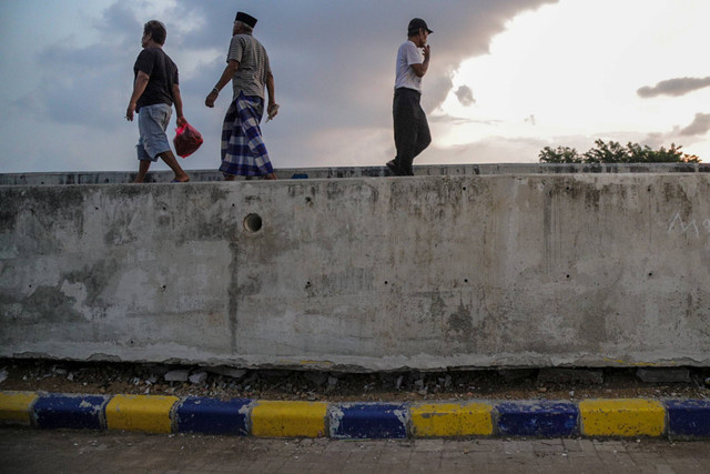 Warga melintas dekat tanggul pengaman pantai yang retak di kawasan pesisir Kalibaru, Cilincing, Jakarta, Sabtu (11/5/2024). Foto: Jamal Ramadhan/kumparan