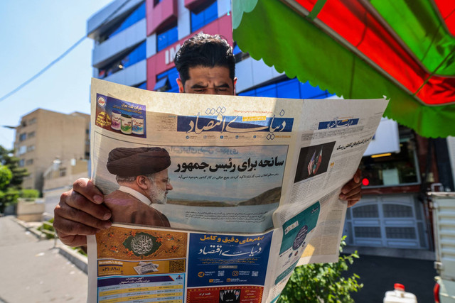 Seorang pria membaca surat kabar dengan laporan halaman depan tentang jatuhnya helikopter presiden Iran di luar kios di Teheran, Iran, Senin (20/5/2024). Foto: Atta Kenare/AFP