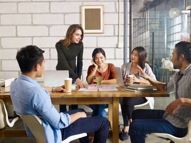 Ilustrasi Teamwork. Sekelompok anak muda duduk di meja di kantor ruang terbuka modern yang cerah. Karyawan muda menjelaskan sesuatu sambil berdiri di depan penonton Sumber: Pixabay.com
