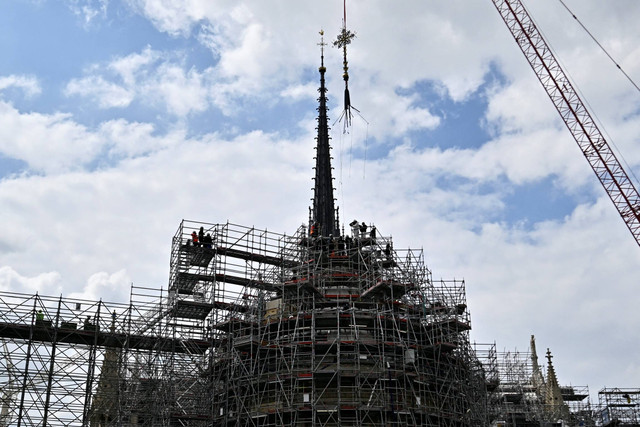 Petugas menggunakan derek untuk memasang kembali salib di apse Katedral Notre Dame de Paris, di Paris, Prancis, Sabtu (24/5/2024). Foto: Julien De Rosa/AFP