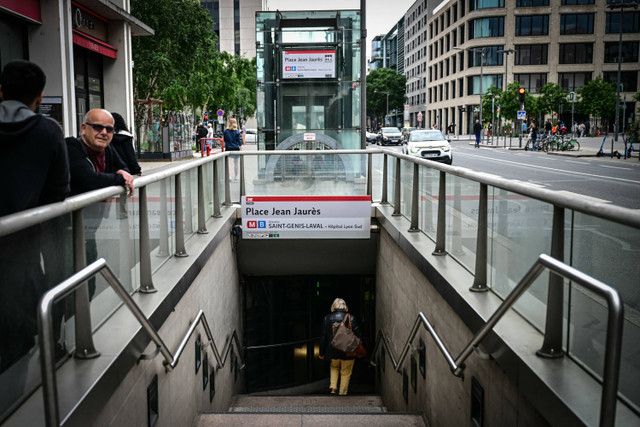 Seorang wanita berjalan menuruni tangga pintu masuk stasiun metro Place Jean Jaures, tempat tiga orang terluka akibat serangan pisau, di Lyon (26/5/2024). Foto: Olivier Chassignole/AFP