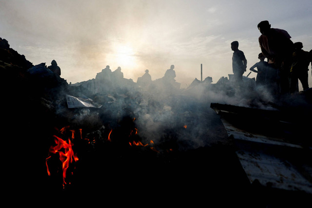 Warga Palestina mencari makanan di antara puing-puing yang terbakar usai serangan Israel di daerah yang diperuntukkan bagi para pengungsi di Rafah, Jalur Gaza selatan, Senin (27/5/2024). Foto: Mohammed Salem / REUTERS