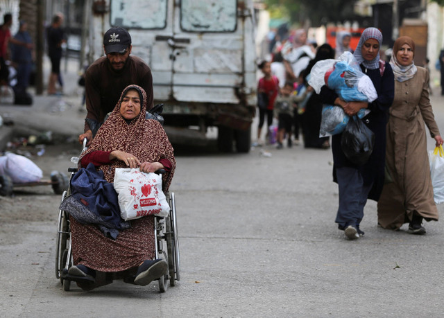 Seorang pria Palestina membantu seorang wanita di kursi roda membawa barang-barangnya saat mereka melakukan perjalanan untuk meninggalkan Rafah akibat operasi militer Israel, di Rafah, di Jalur Gaza selatan (28/5/2024). Foto: Hatem Khaled/REUTERS