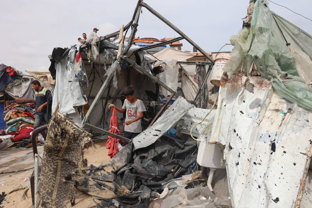 Seorang anak laki-laki Palestina mencari puing-puing di lokasi serangan Israel sehari sebelumnya di sebuah kamp pengungsi di Rafah di Jalur Gaza selatan (28/5/2024). Foto: EYAD BABA/AFP