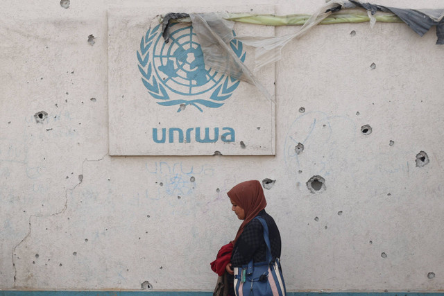 Seorang wanita Palestina berjalan melewati tembok rusak berlogo UNRWA di sebuah kamp pengungsi internal di Rafah di Jalur Gaza selatan (28/5/2024). Foto: EYAD BABA/AFP