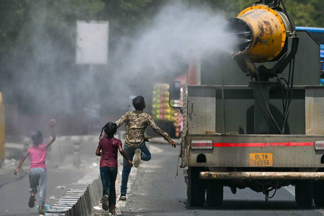 Anak-anak berlarian di belakang truk yang menyemprotkan air di sepanjang jalan pada hari musim panas di New Delhi pada 28 Mei 2024.  Foto: Arun SANKAR / AFP