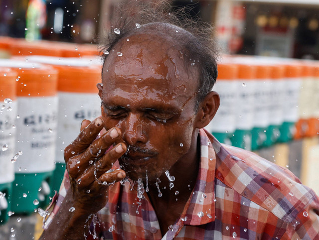 Seorang pria menyemprotkan air dingin ke wajahnya dari toples air saat gelombang panas di Ahmedabad, India, 29 Mei 2024. Foto: Reuters/Amit Dave