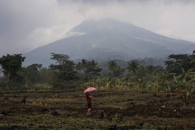 Seorang warga memegang payung berdiri di dekat rumah mereka di kaki gunung berapi Gunung Kanlaon di sebuah desa di La Castellana, provinsi Negros Occidental, Filipina tengah pada Selasa (4/6/2024), sehari setelah gunung berapi tersebut meletus. Foto: FERDINAND EDRALIN/AFP