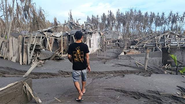 Seorang warga berjalan di atas sisa endapan lahar dingin sambil melihat bangunan rumah yang rusak akibat erupsi Gunung Ruang. (foto: febry kodongan/manadobacirita)