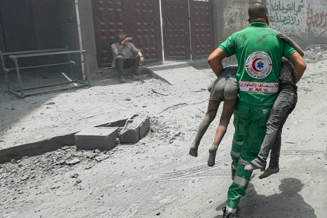 Seorang petugas penyelamat Palestina membawa korban di lokasi serangan Israel terhadap rumah-rumah di kamp pengungsi Al Shati di Kota Gaza, Sabtu (22/6/2024). Foto: Ayman Al Hassi/REUTERS