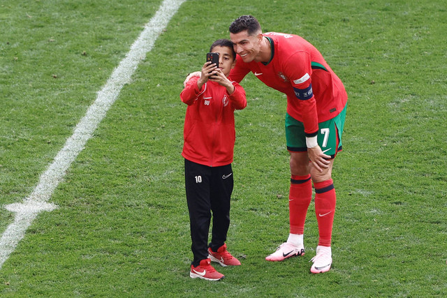 Cristiano Ronaldo (kanan) layani selfie bocah yang menyusup saat Turki vs Portugal dalam matchday kedua Grup F Piala Eropa 2024 di Signal Iduna Park, Jerman, pada Sabtu (22/6) malam WIB. Foto: KENZO TRIBOUILLARD / AFP