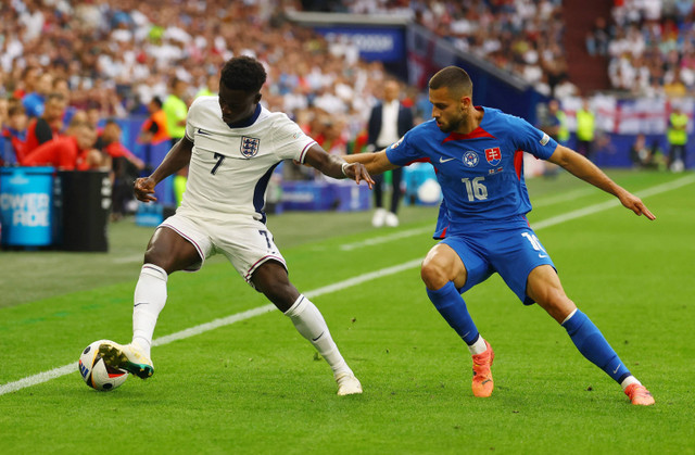 Pemain Inggris Bukayo Saka beraksi dengan pemain Slovakia David Hancko saat pertandingan Inggris melawan Slovakia pada Piala Eropa 2024 di Arena AufSchalke, Gelsenkirchen, Jerman, Minggu (30/6/2024). Foto: Kai Pfaffenbach/REUTERS