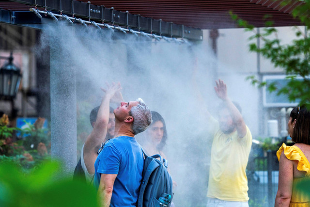 Seorang pria mendinginkan diri di bawah hujan kabut di pusat kota Tokyo, Jepang, Senin (8/7/2024). Foto: Kazuhiro NOGI / AFP