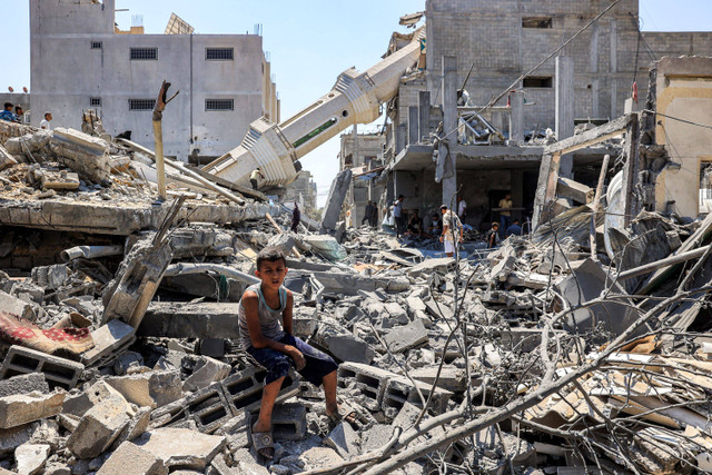 Seorang anak duduk di puing-puing puing-puing bangunan yang hancur di dekat menara masjid yang roboh di Nuseirat, Jalur Gaza, Rabu (17/7/2024). Foto: Eyad BABA / AFP