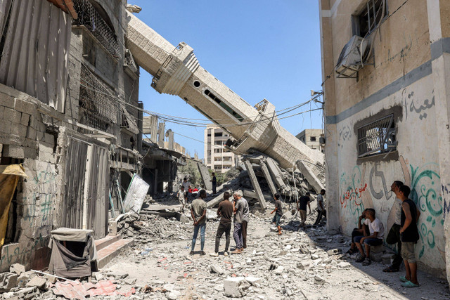 Warga Palestina berdiri di dekat menara masjid yang roboh di Nuseirat, Jalur Gaza, Rabu (17/7/2024). Foto: Eyad BABA / AFP