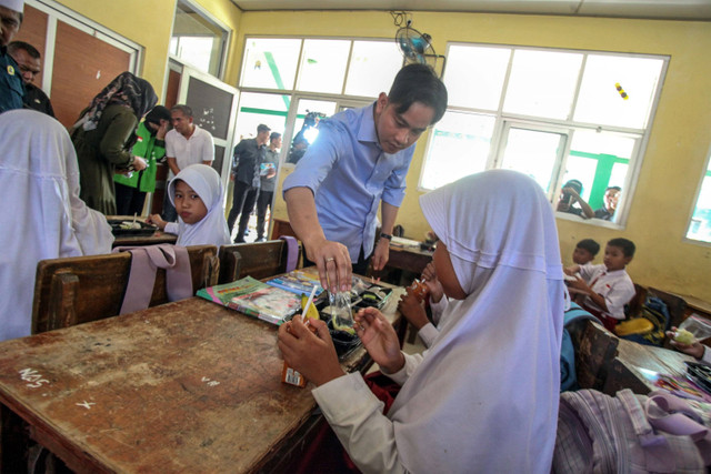 Wakil Presiden terpilih Gibran Rakabuming Raka membantu siswa membuka paket makanan saat meninjau uji coba pelaksanaan program makan bergizi gratis di SDN Sentul 03,  Kabupaten Bogor, Jawa Barat, Selasa (23/7/2024).  Foto: Yulius Satria Wijaya/ANTARA FOTO