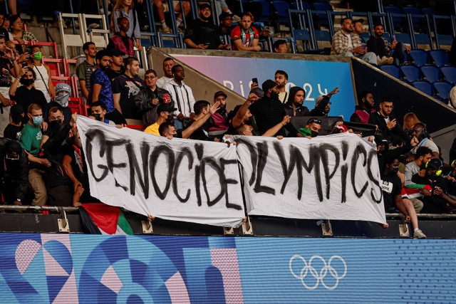 Penonton memegang spanduk bertuliskan "Olimpiade Genosida" saat pertandingan  grup D Olimpiade Paris 2024 antara Israel dan Paraguay di Parc des Princes, Paris, Prancis, Sabtu (27/7/2024). Foto: Aurelien Morissard/AP Photo