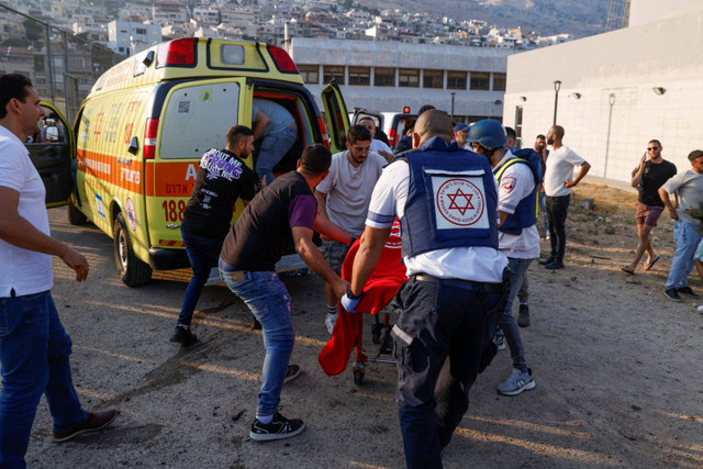 Pasukan keamanan Israel dan petugas medis mengangkut korban bersama dengan penduduk setempat, di sebuah lokasi di mana serangan yang dilaporkan dari Lebanon jatuh di desa Majdal Shams di wilayah Golan yang diserang Israel (28/7/2024). Foto: JALAA MAREY / AFP