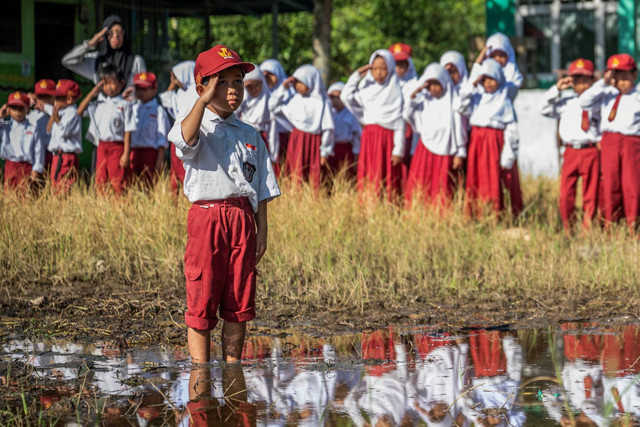 Sejumlah siswa melakukan penghormatan saat upacara bendera di halaman yang tergenang air dan berlumpur di SD Negeri Basirih 10, Banjarmasin, Kalimantan Selatan, Senin (29/7/2024). Foto: Bayu Pratama S/ANTARA FOTO